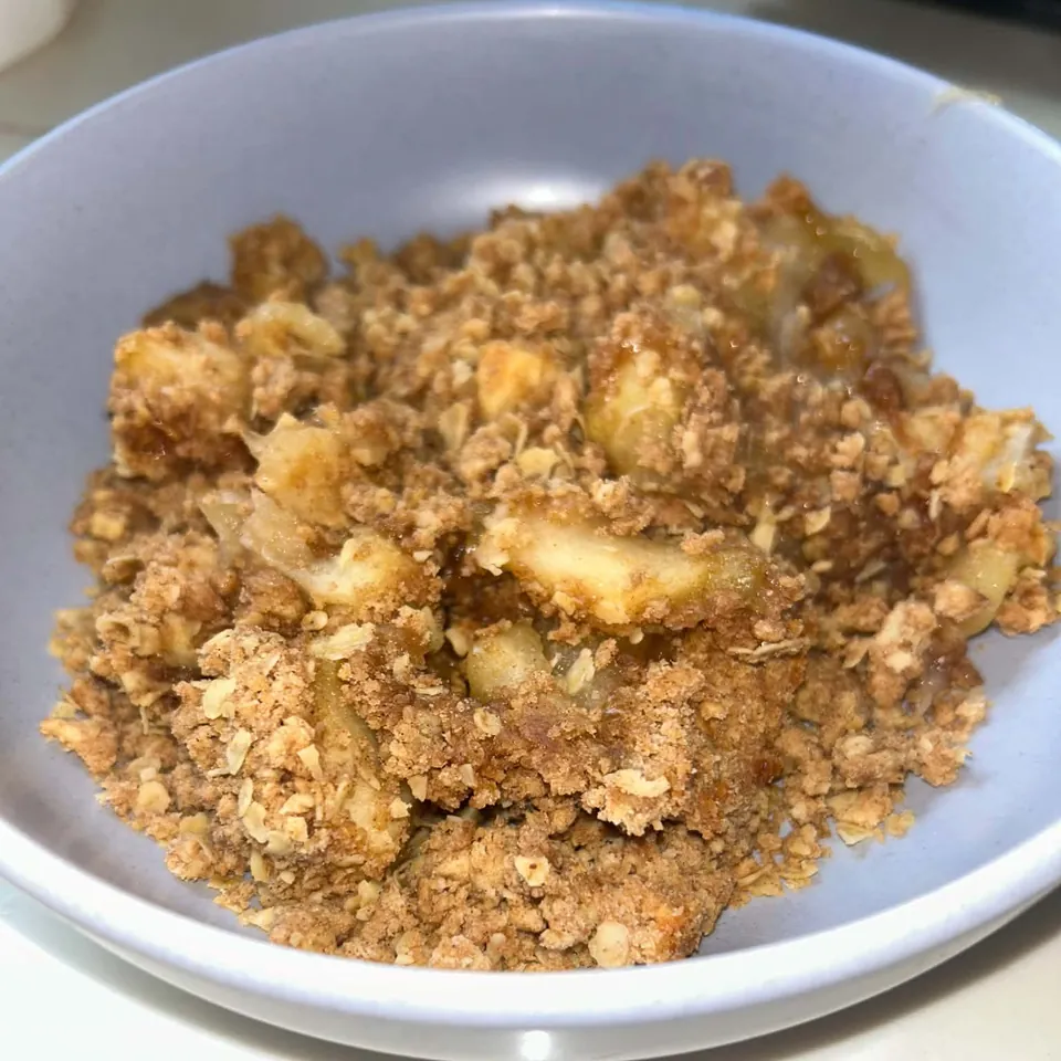 Golden apple crumble with a crisp, crumbly topping served in a pale blue bowl